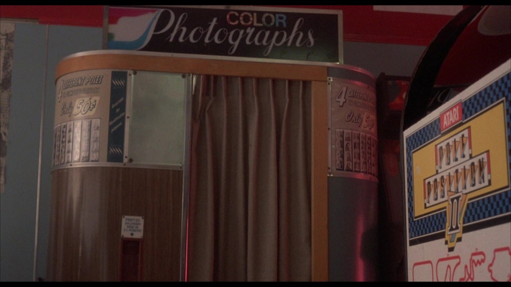 A vintage color photograph booth with a wooden exterior and a curtain, featuring a sign that advertises 'Color Photographs' and pricing details.