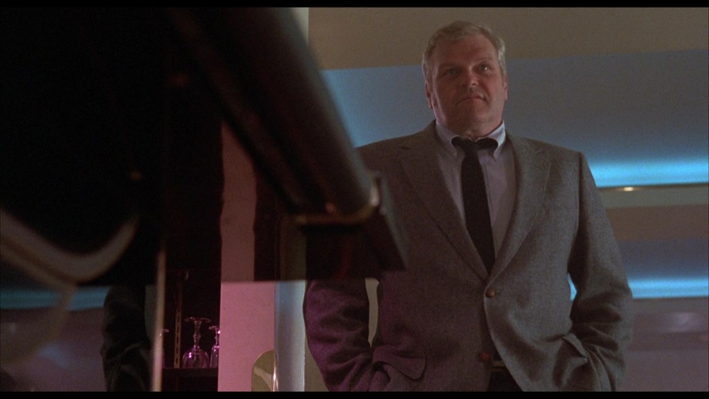 A middle-aged man in a grey suit stands confidently, looking towards the camera in a modern setting with soft lighting.