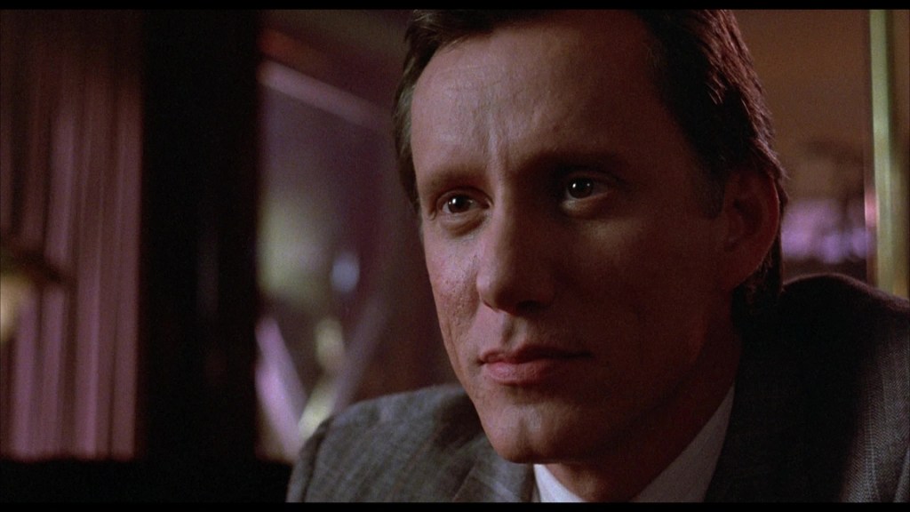 Close-up of a man with short hair and a thoughtful expression, sitting in a dimly lit environment.