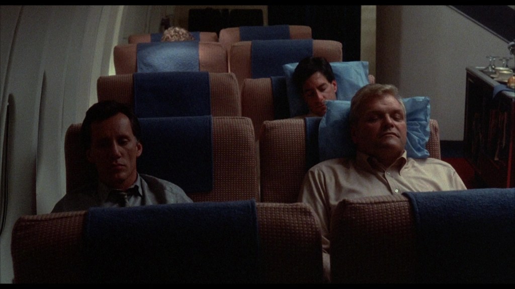 Passengers resting on an airplane with seat backs reclined and blue pillows.