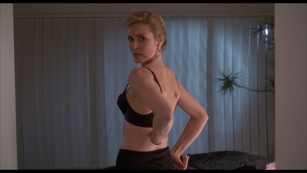 Woman in a black bra looking over her shoulder in a softly lit bedroom.