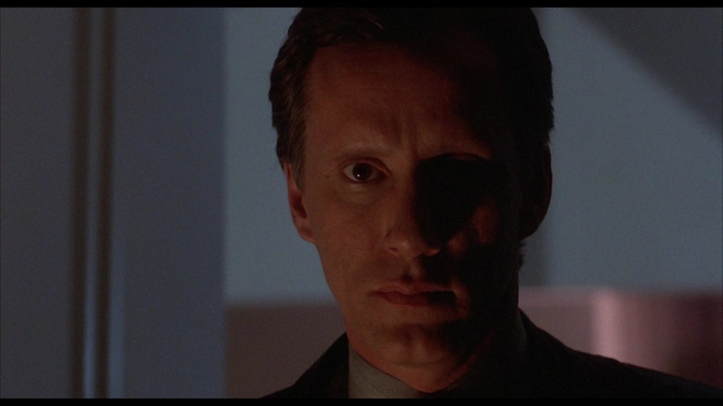 Close-up of a man with a serious expression, illuminated from one side, creating dramatic shadows on his face.