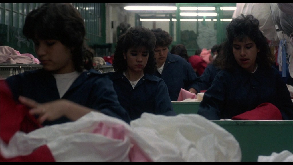 A group of young women working in a laundry facility, folding and sorting colorful fabric. They wear dark uniforms and appear focused on their tasks.