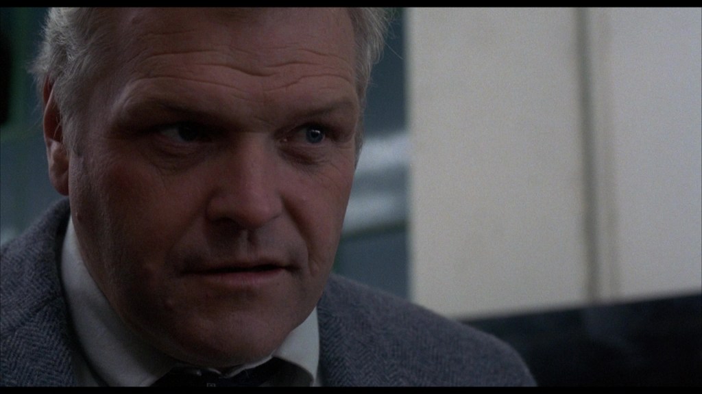 Close-up of a serious older man with gray hair, wearing a suit and looking intently off-camera.