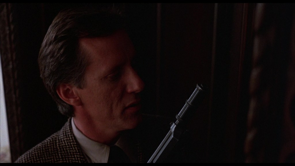 Close-up of a man holding a gun near a doorframe, with a serious expression on his face.