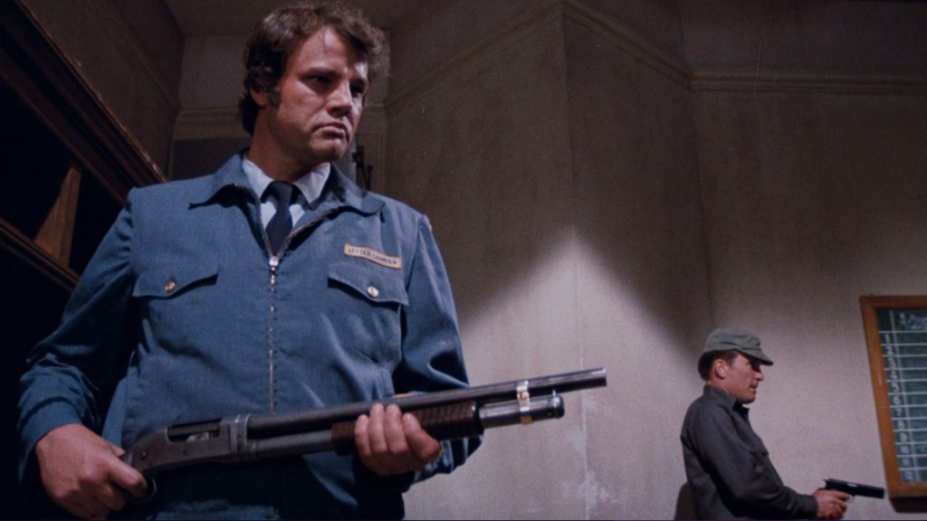 Two men in armed standoff inside a building, one wearing a blue uniform and holding a shotgun, the other in military attire with a sidearm.