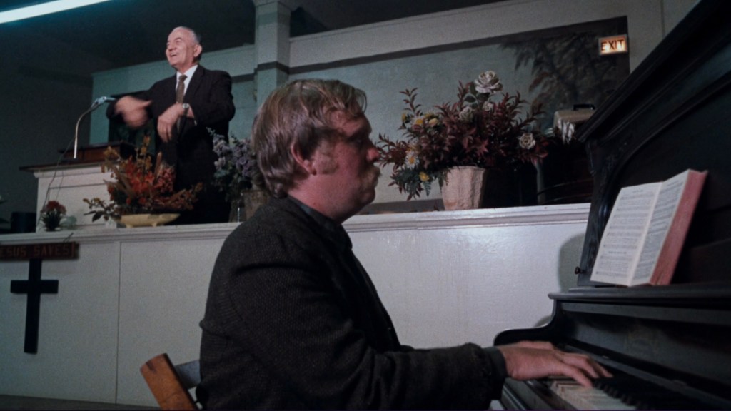 A man playing piano at a church service while another man gestures enthusiastically at the podium.