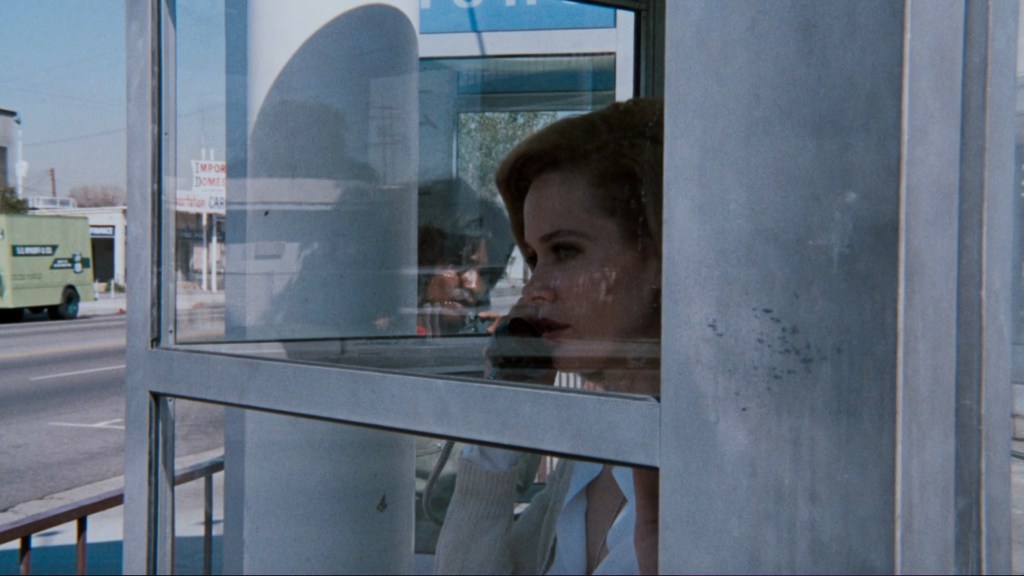A woman talking on the phone inside a telephone booth, with a city street visible in the background.