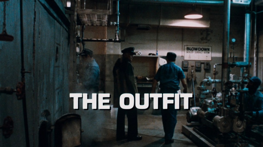 Scene from 'The Outfit' featuring characters in an industrial setting with machinery and pipes.