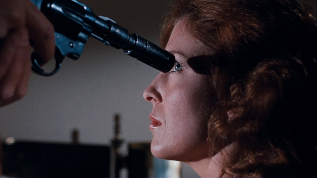 Close-up of a woman with red hair facing a handgun pointed at her face.