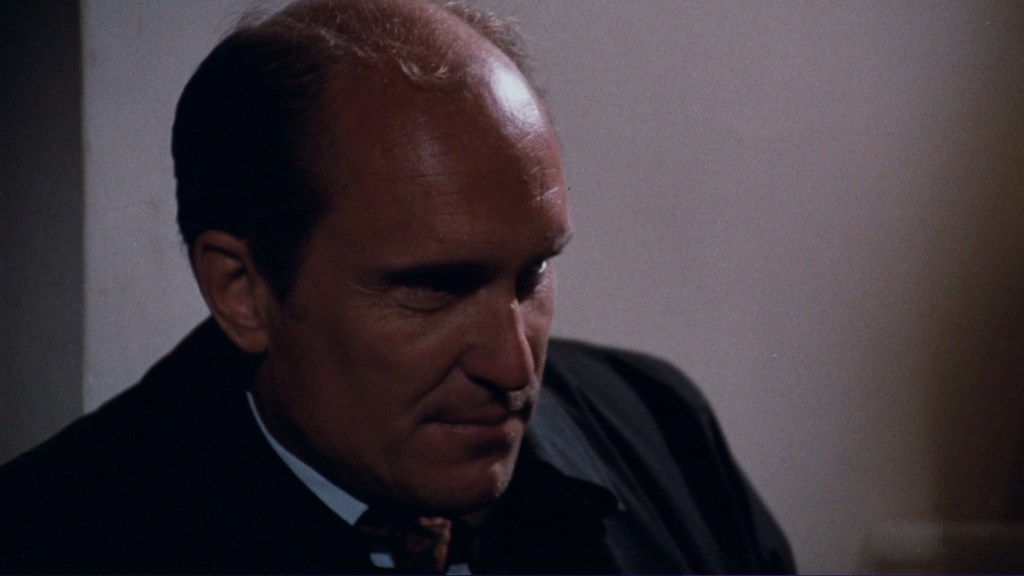 A close-up of a man's profile, featuring a balding head and a focused expression against a blurred background.