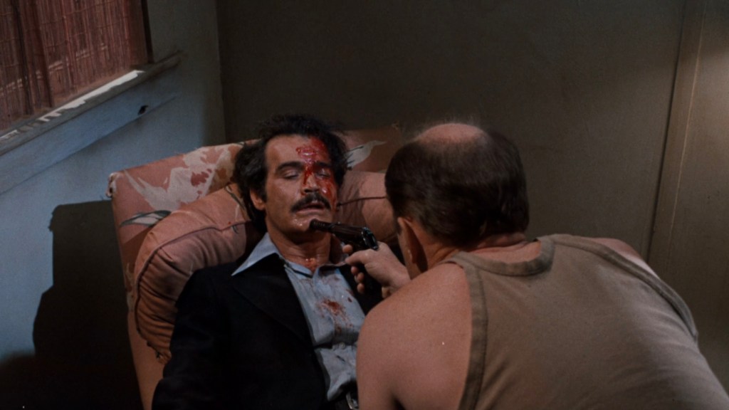A tense scene depicting a man seated in a chair with a gun pointed at him by another man leaning over him. The seated man has blood on his face and appears distressed, while the other man seems determined.
