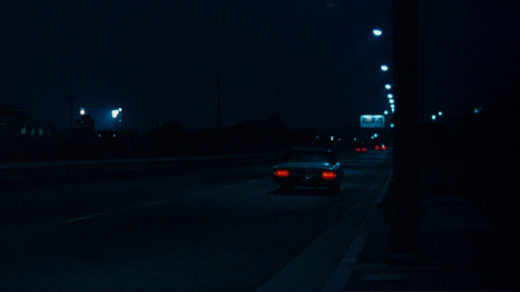 A car driving down a dark street illuminated by streetlights at night.