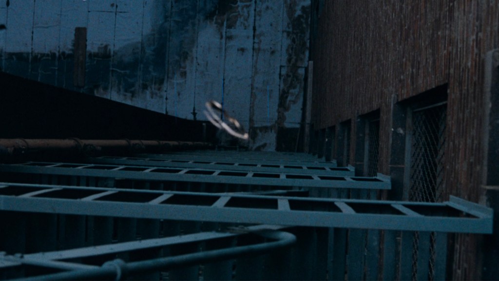 Close-up of a flying object above a series of metal grates against a textured wall at dusk.