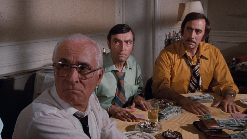 Three men seated at a table covered with stacks of money and drinks, discussing a serious matter.