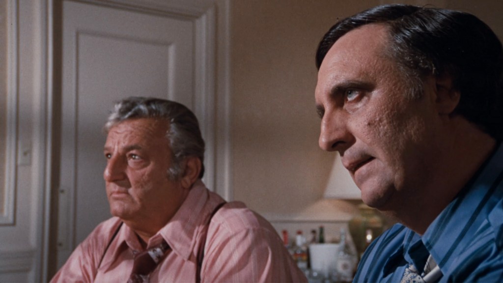 Two men sitting at a table, deep in conversation, one wearing a pink shirt and the other in a blue shirt.