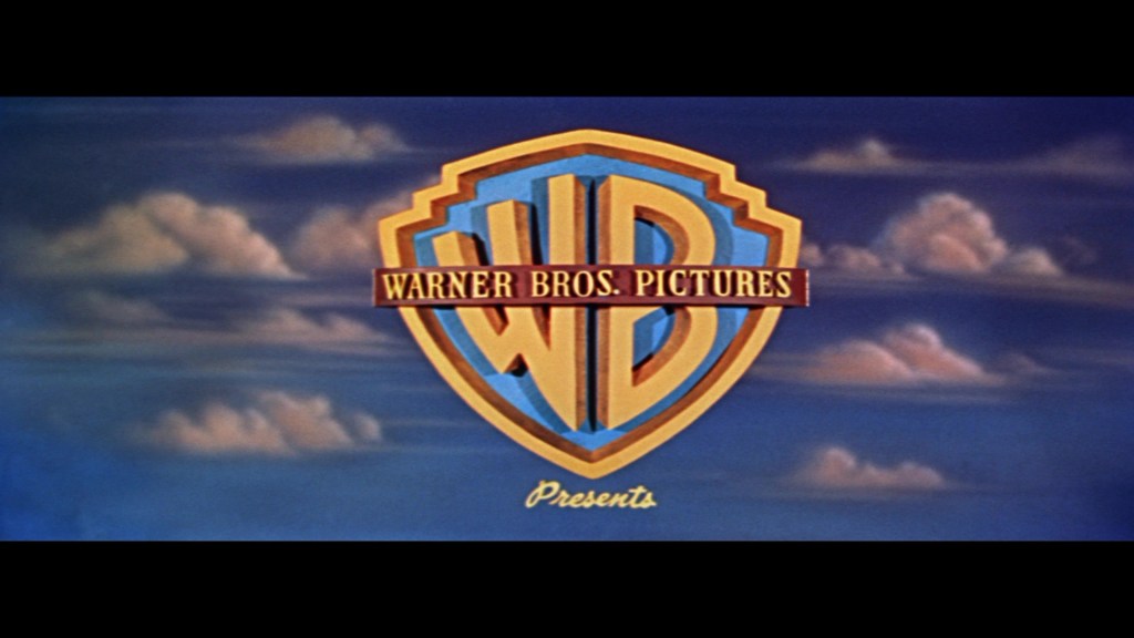 The Warner Bros. Pictures logo featuring the initials 'WB' in a shield, set against a blue sky with clouds.