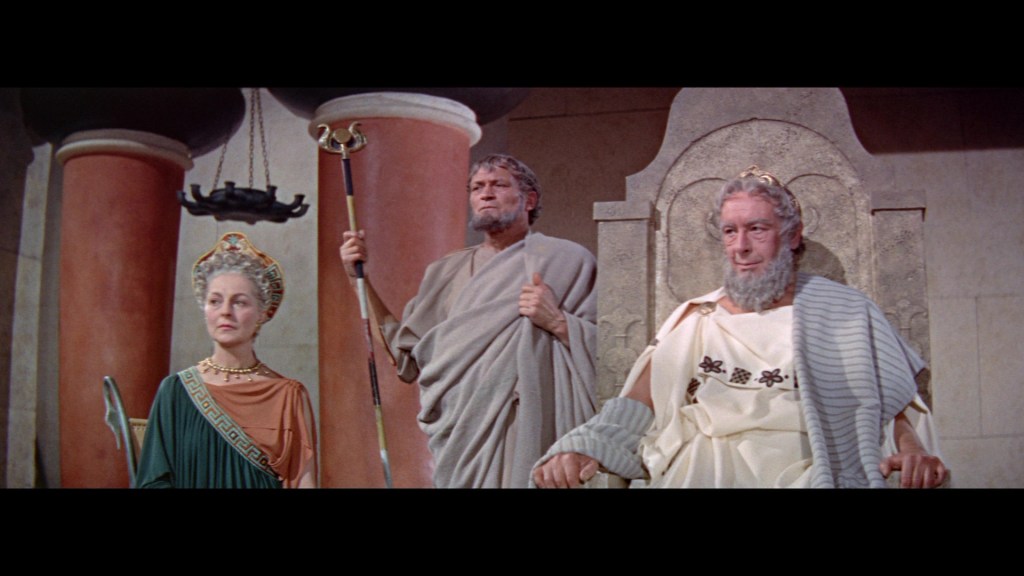 Three ancient Greek figures stand in a classical setting, with one seated on a throne. They are dressed in traditional garb, suggesting a scene of authority and wisdom.