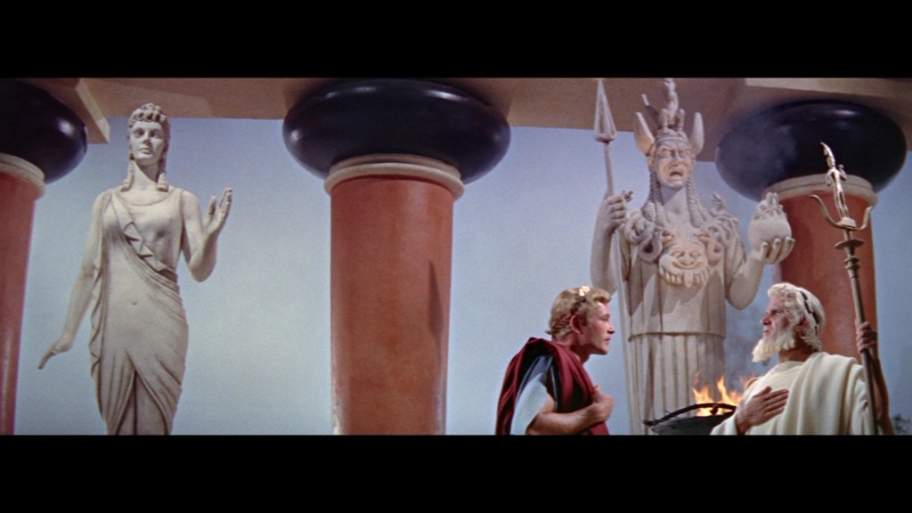 A dramatic scene featuring two figures in ancient Greek attire conversing, with large statues of Greek deities in the background, including one holding a spear and another in a flowing robe.