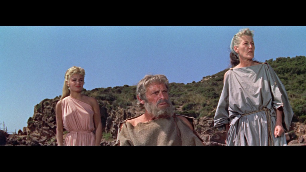 A scene depicting three characters on a rocky beach, one man with a beard seated in the center, flanked by two women in ancient-style clothing, with a clear blue sky in the background.