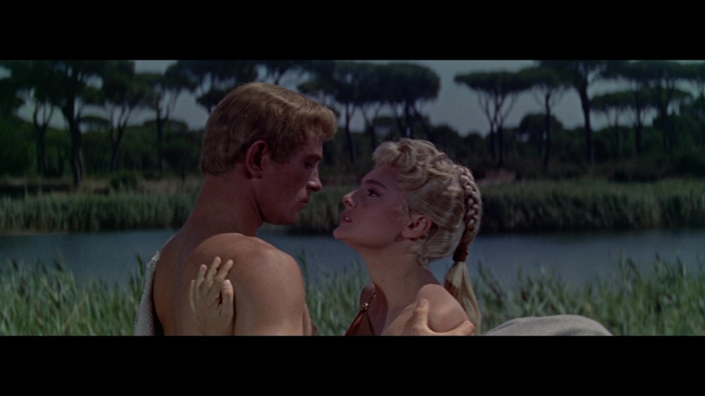 A romantic scene featuring a man and woman close together, set near a body of water surrounded by lush greenery.