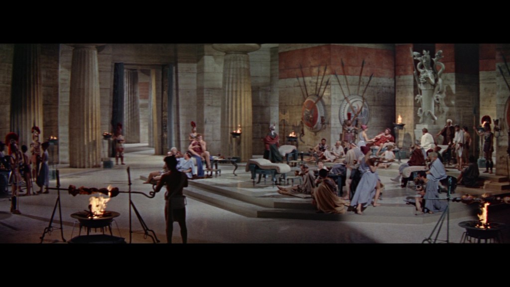 A grand ancient setting with pillars and sculptures, featuring a group of people in historical attire engaging in various activities. Some individuals are seated and conversing, while others are standing nearby, with torches and elaborate decorations enhancing the atmosphere.