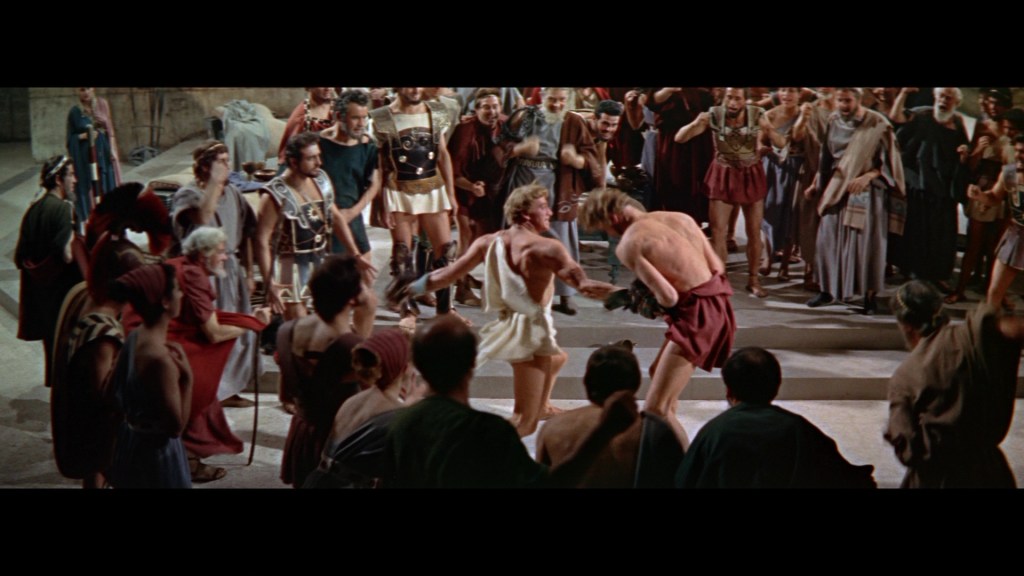 A crowd of ancient Romans watches two gladiators engaged in a fierce battle in a large arena.