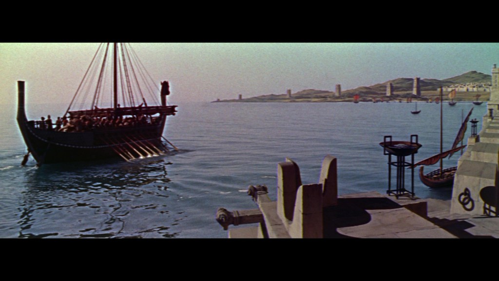 A large ancient ship is sailing on calm waters, with a mountainous coastline in the background. The ship has multiple oars and a figure standing at the prow, while smaller boats are depicted nearby.