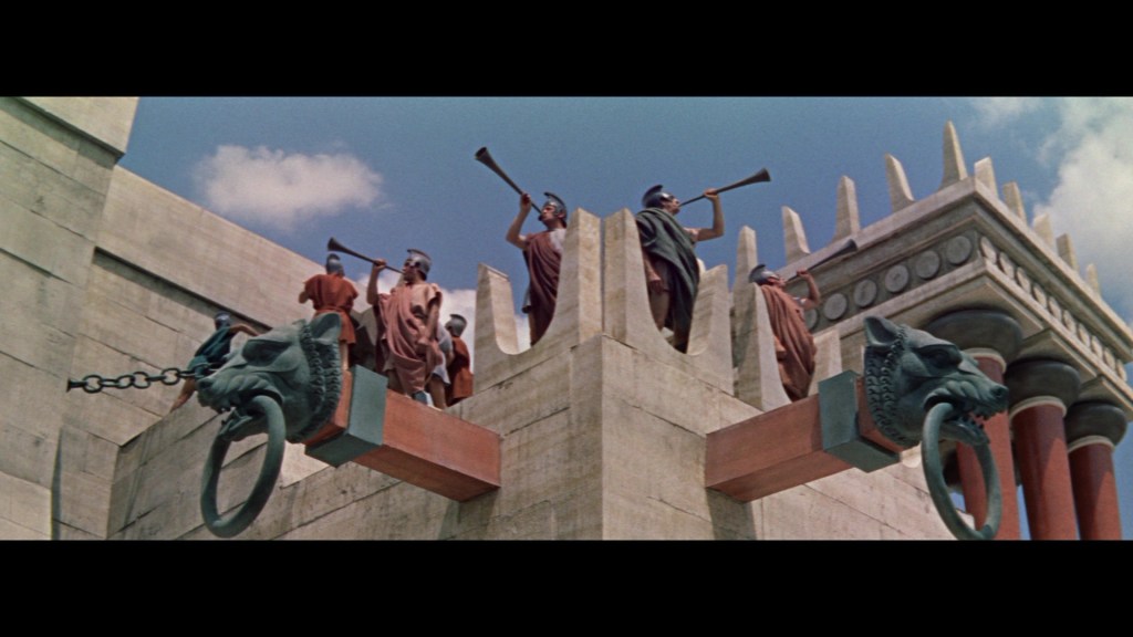 A scene depicting ancient soldiers playing horns while standing on top of a grand architectural structure, featuring decorative lion heads and columns against a blue sky.