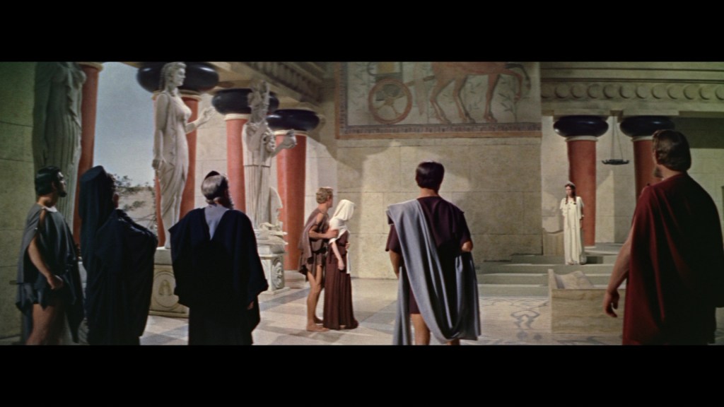 A group of ancient Greek figures dressed in robes stands in an elaborately decorated interior, featuring statues and frescoes on the walls.