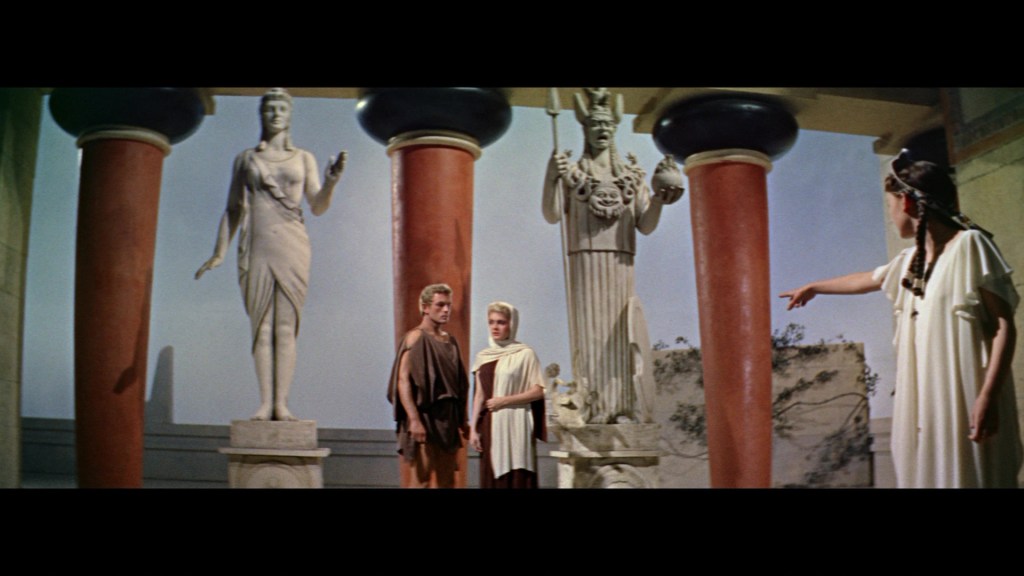Scene depicting three ancient Greek statues and two individuals conversing in a classical setting, with columns and decorative elements in the background.