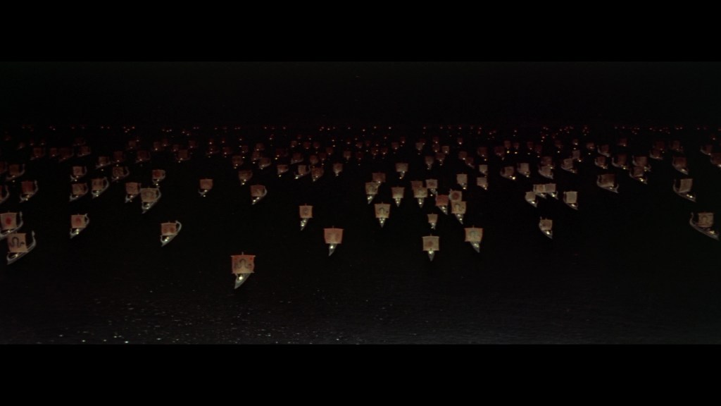 A dark scene featuring numerous small boats with illuminated sails, creating a mesmerizing pattern on the water.