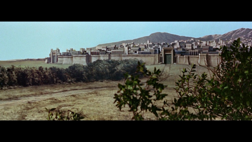 A panoramic view of a walled city surrounded by hills and greenery, showcasing its architectural features and fortress-like appearance.