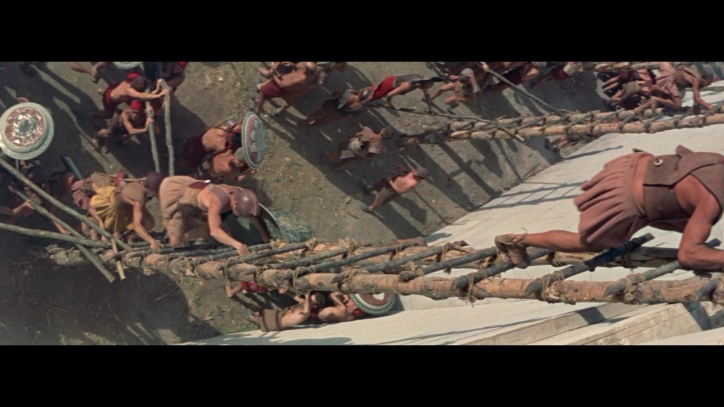 Aerial view of ancient soldiers climbing wooden ladders towards a fortress, with warriors and shields visible in the surrounding area.