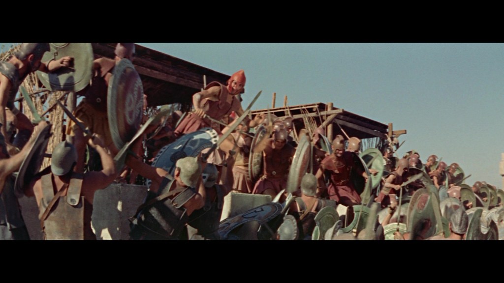 A group of ancient warriors in armor and helmets brandishing shields and weapons, preparing for battle in a historical setting.