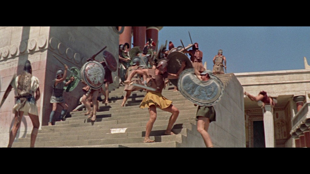A chaotic battle scene on stone steps, featuring ancient soldiers in armor wielding weapons and shields.