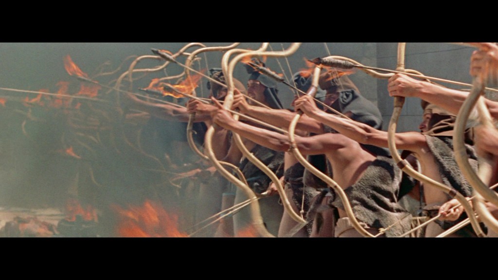 Group of archers aiming bows with flaming arrows, set against a backdrop of smoke and fire.