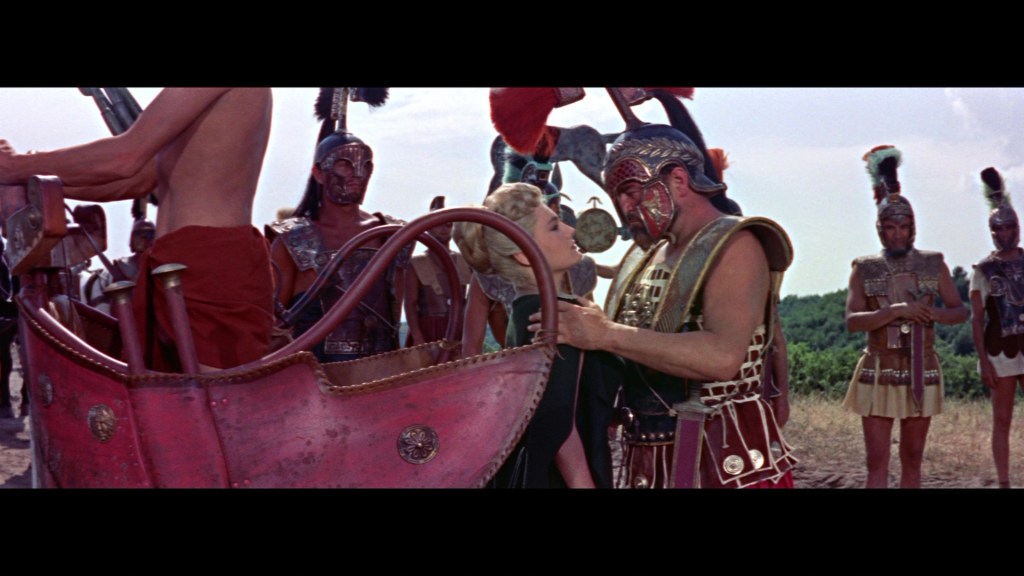 A scene depicting a dramatic moment between a warrior and a woman, surrounded by ancient soldiers and a chariot.