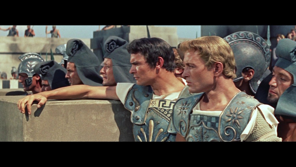 Group of ancient warriors in ornate armor, watching an event, with a focus on two men in the foreground.