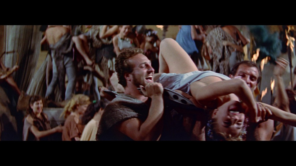 A chaotic scene from a historical film featuring a group of people celebrating, with one man joyfully lifting a woman in a dramatic manner while others surround them energetically.