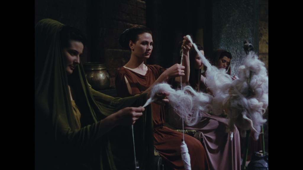 Four women in historical attire are engaged in spinning fibers into thread, with a focus on their hands and the wool they are working with.
