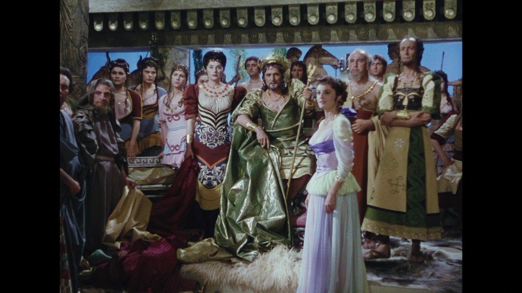 A scene depicting a group of ancient Roman characters gathered around a central figure in a regal outfit, showcasing elaborate costumes and a dramatic atmosphere.