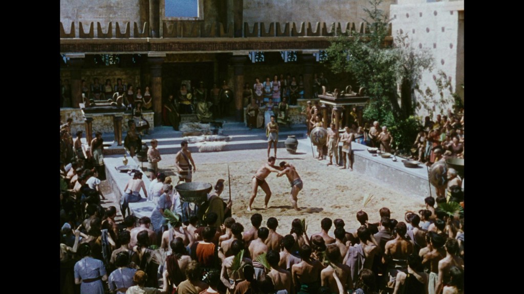 A crowd watches a wrestling match in an ancient amphitheater, surrounded by spectators in traditional clothing and architectural features of classical design.