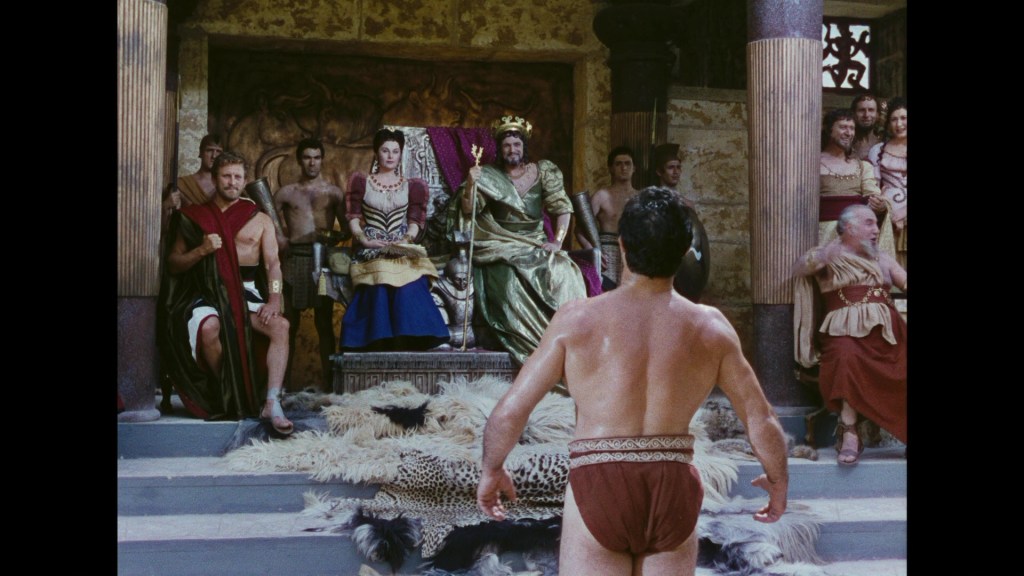 A scene depicting a group of ancient Roman figures in a grand hall, with a king seated on a throne and individuals in various garments, including a man standing barefoot in a loincloth facing the throne.