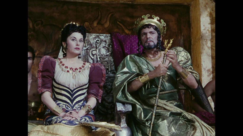 A regal woman in an elaborate dress and a man in royal attire sit on a throne, with the woman wearing a crown and the man holding a scepter.