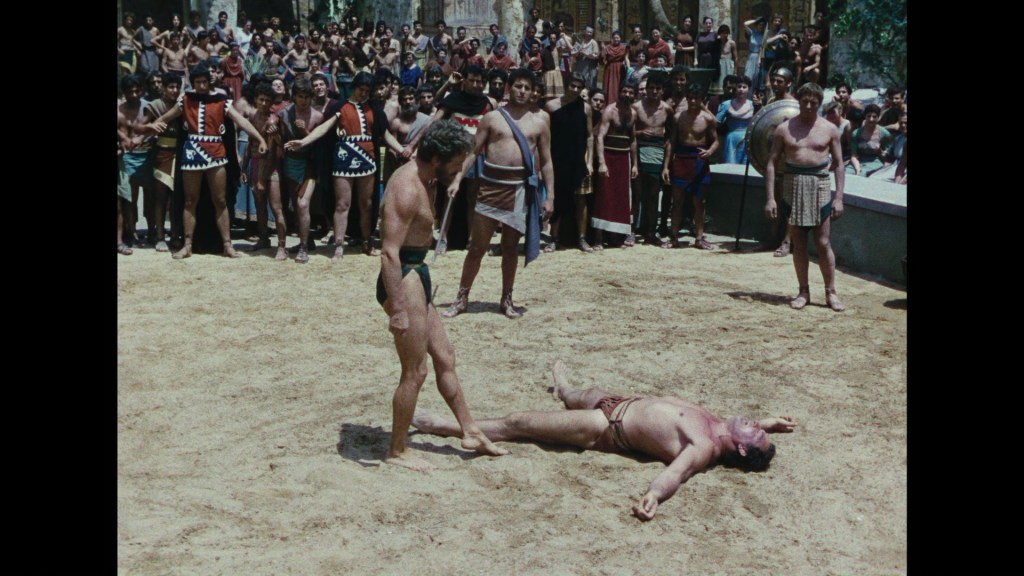 A gladiatorial arena with a defeated fighter lying on the ground, while another fighter stands over him. Surrounding them is a crowd of spectators in ancient attire, cheering or reacting to the event.