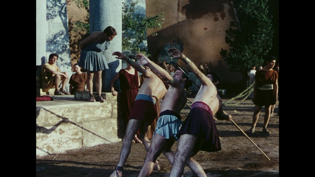 Two male athletes engaged in a wrestling match outdoors, surrounded by spectators in ancient Greek attire.