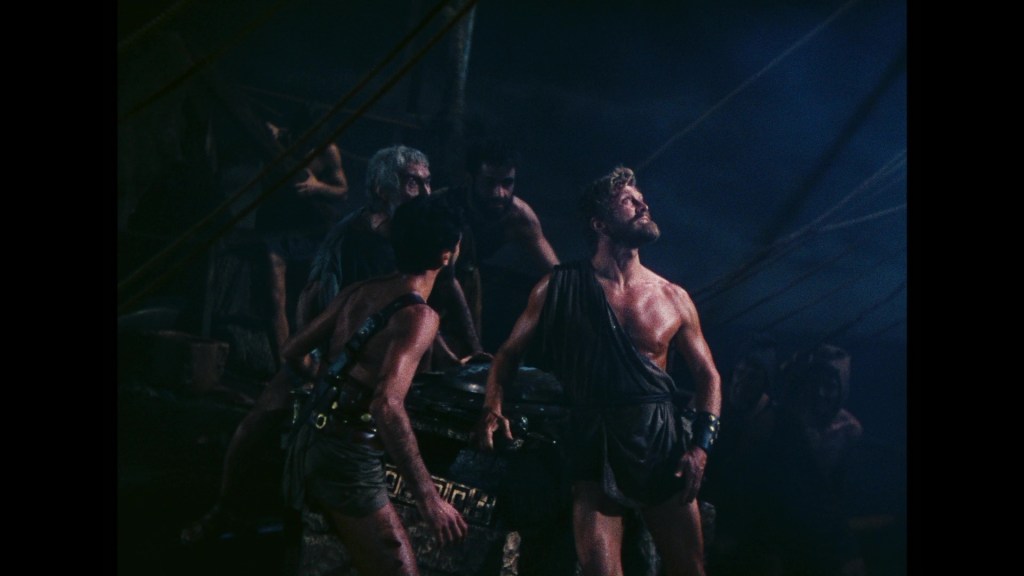 A group of ancient Greek men on a ship, some standing and others partially obscured, with dramatic lighting creating a tense atmosphere.