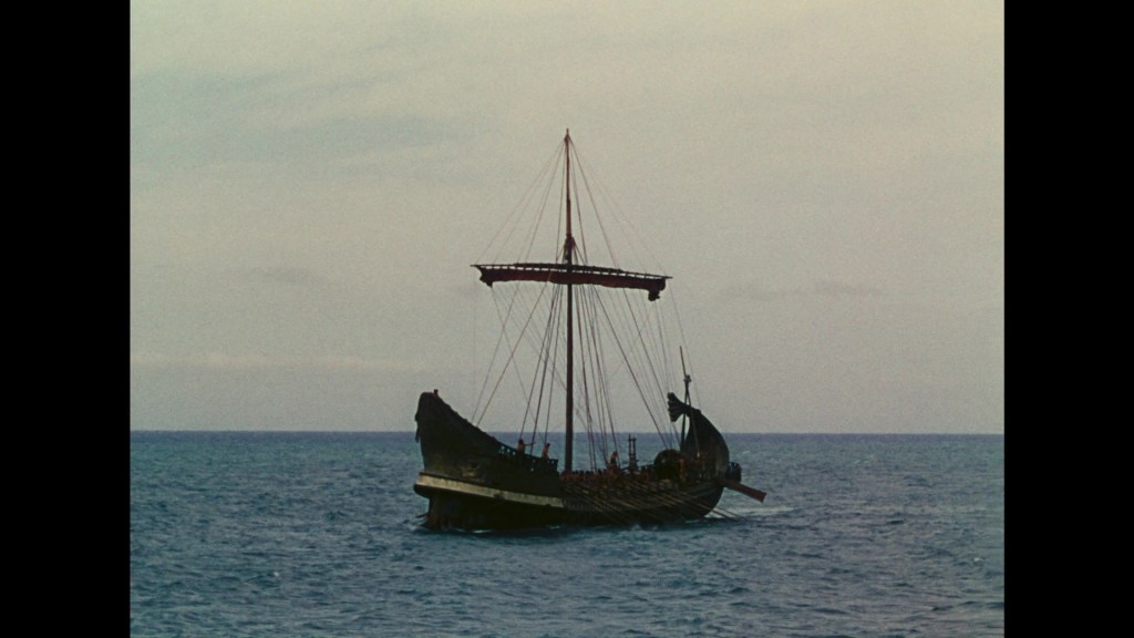 A traditional sailing ship anchored on calm waters, with a clear sky and gentle waves in the background.