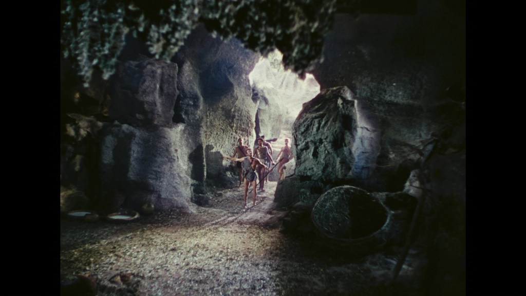 A prehistoric scene depicting early humans walking through a cave with rocky formations and primitive tools.